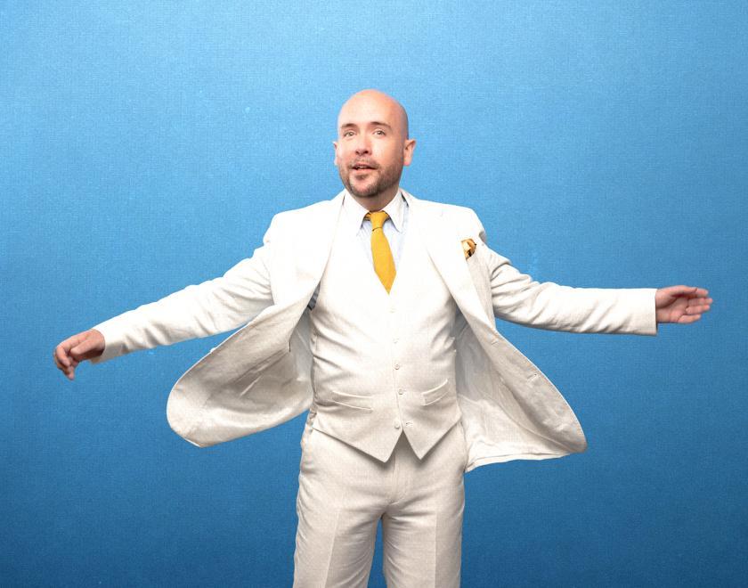 Tom Allen in a white suit in front of a blue backdrop