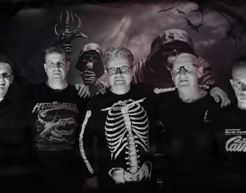 The band Vampire Strikers, five middle-aged men wearing black. The one in the middle has a skeleton printed on his jumper.